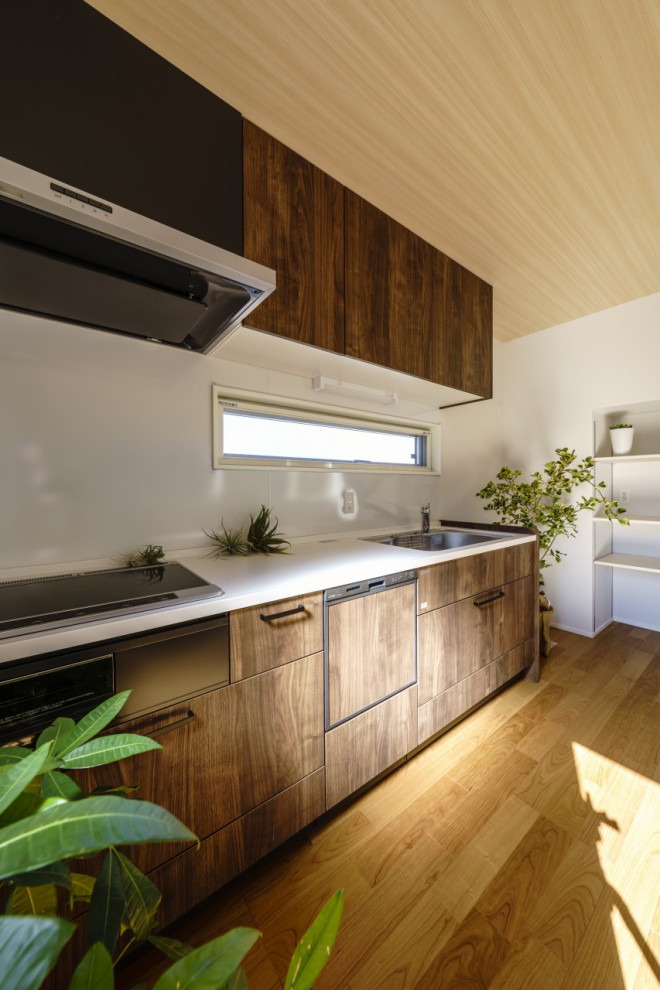 Modelo de cocina lineal moderna de tamaño medio cerrada con puertas de armario marrones, encimera de acrílico, salpicadero blanco, suelo de madera clara, suelo marrón y papel pintado