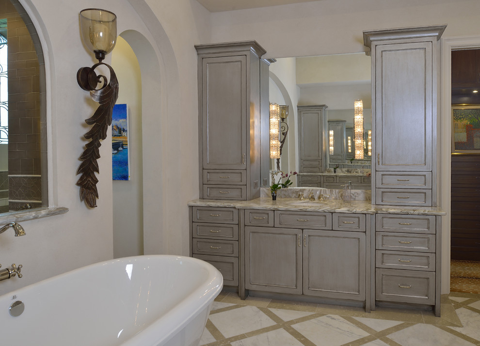 Photo of a large eclectic master bathroom in Houston with recessed-panel cabinets, grey cabinets, a freestanding tub, a double shower, gray tile, ceramic tile, beige walls, porcelain floors, an undermount sink, marble benchtops, beige floor and a hinged shower door.