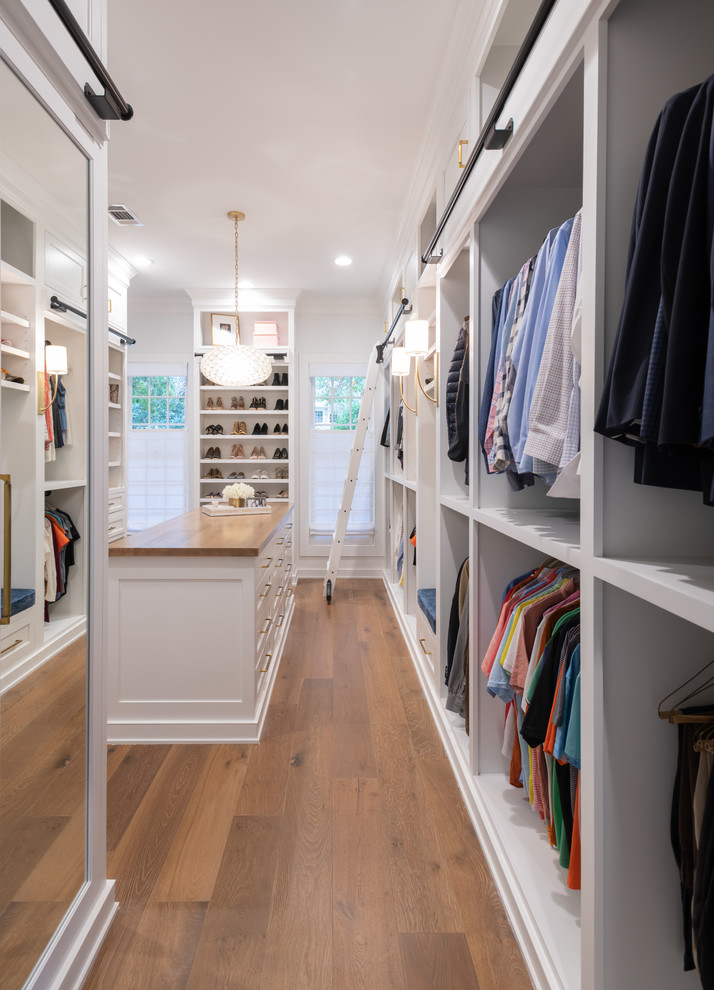 This is an example of a country gender-neutral walk-in wardrobe in Houston with open cabinets, white cabinets, medium hardwood floors and brown floor.