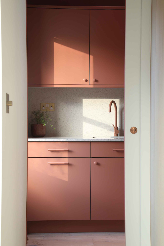 This is an example of a mid-sized scandinavian single-wall utility room in Other with an integrated sink, flat-panel cabinets, red cabinets, quartzite benchtops, multi-coloured splashback, engineered quartz splashback, light hardwood floors and multi-coloured benchtop.
