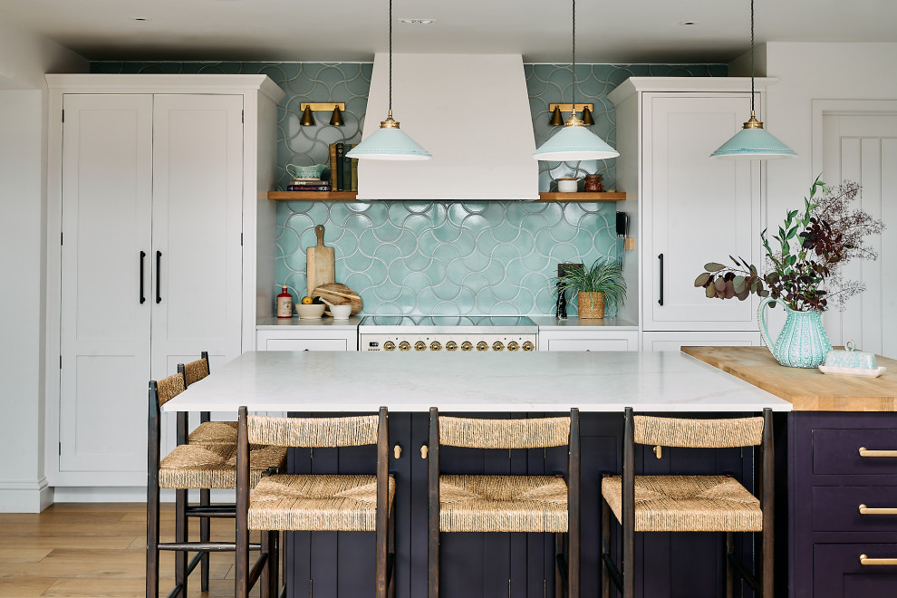 This is an example of a medium sized country kitchen/diner in Berkshire with shaker cabinets, white cabinets, engineered stone countertops, blue splashback, ceramic splashback, integrated appliances, medium hardwood flooring, an island, brown floors, white worktops and feature lighting.