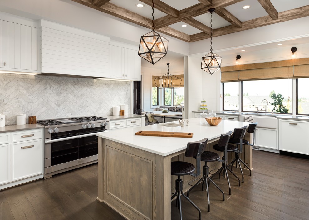 Photo of a large country u-shaped kitchen in Orange County with a farmhouse sink, flat-panel cabinets, white cabinets, quartz benchtops, white splashback, limestone splashback, stainless steel appliances, dark hardwood floors, with island and brown floor.