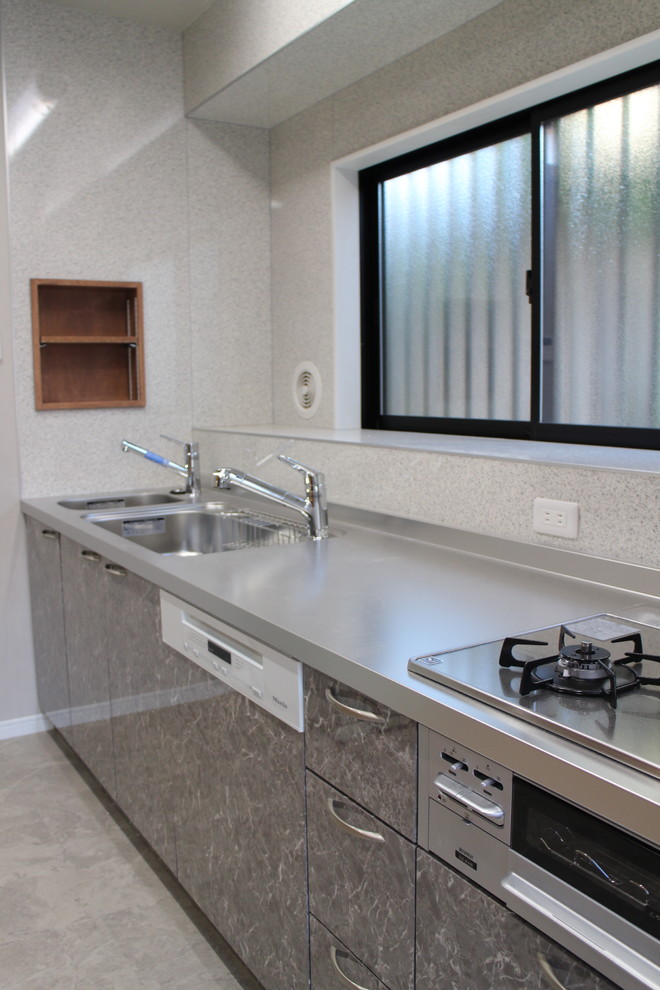 Photo of a large asian single-wall kitchen in Other with a triple-bowl sink, flat-panel cabinets, grey cabinets, stainless steel benchtops, white splashback, linoleum floors and grey floor.