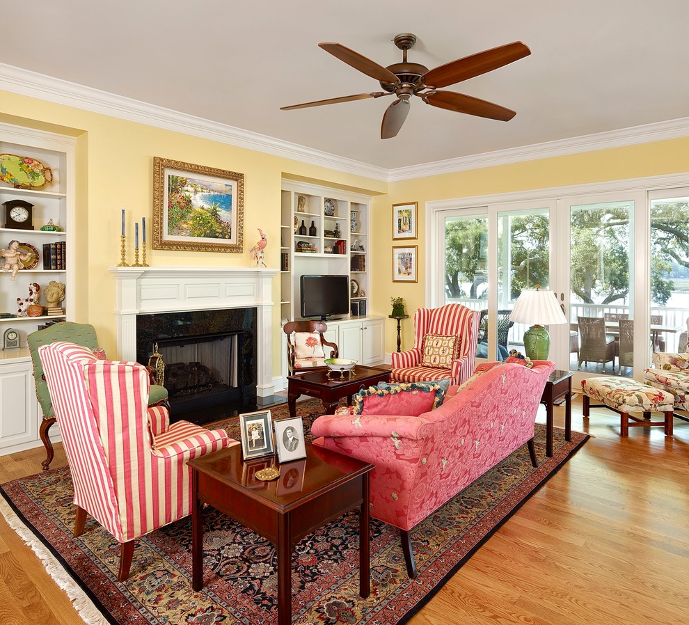 This is an example of a traditional formal open concept living room in Charleston with a freestanding tv, yellow walls, light hardwood floors and a stone fireplace surround.