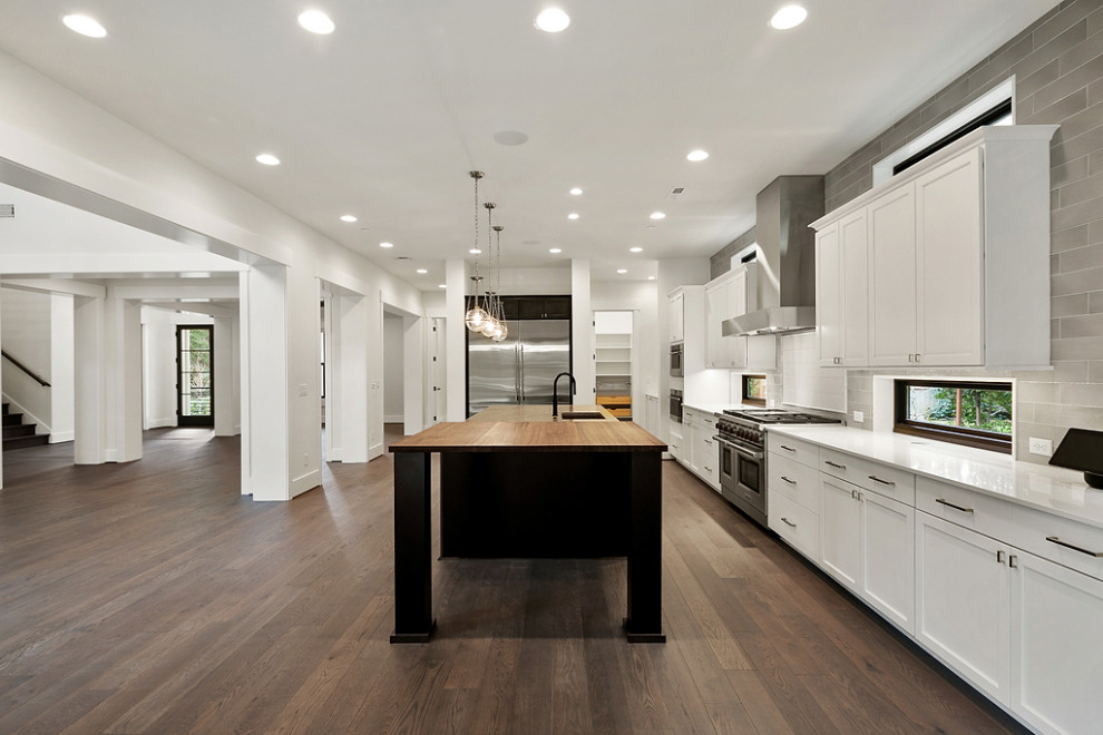 Design ideas for a large country galley kitchen/diner in Seattle with a built-in sink, recessed-panel cabinets, white cabinets, engineered stone countertops, grey splashback, metro tiled splashback, stainless steel appliances, dark hardwood flooring, an island, brown floors and white worktops.
