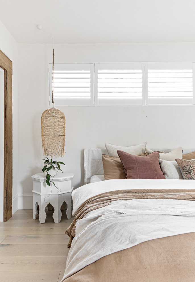 Large beach style guest bedroom in Sydney with white walls, light hardwood floors and brown floor.