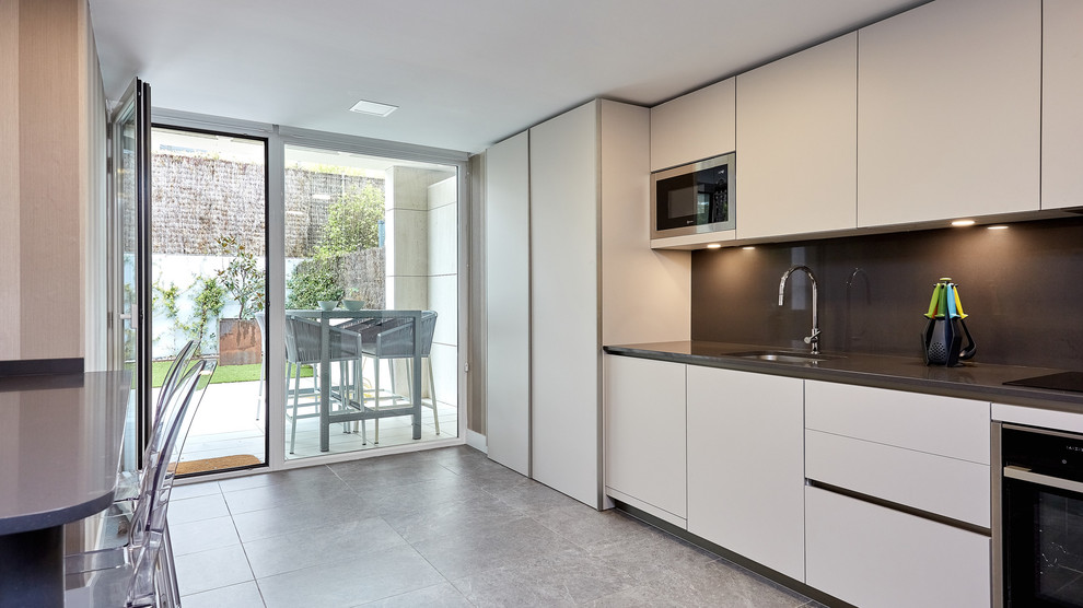 This is an example of a large transitional single-wall separate kitchen in Madrid with a single-bowl sink, white cabinets, black splashback, stainless steel appliances, no island, grey floor and black benchtop.