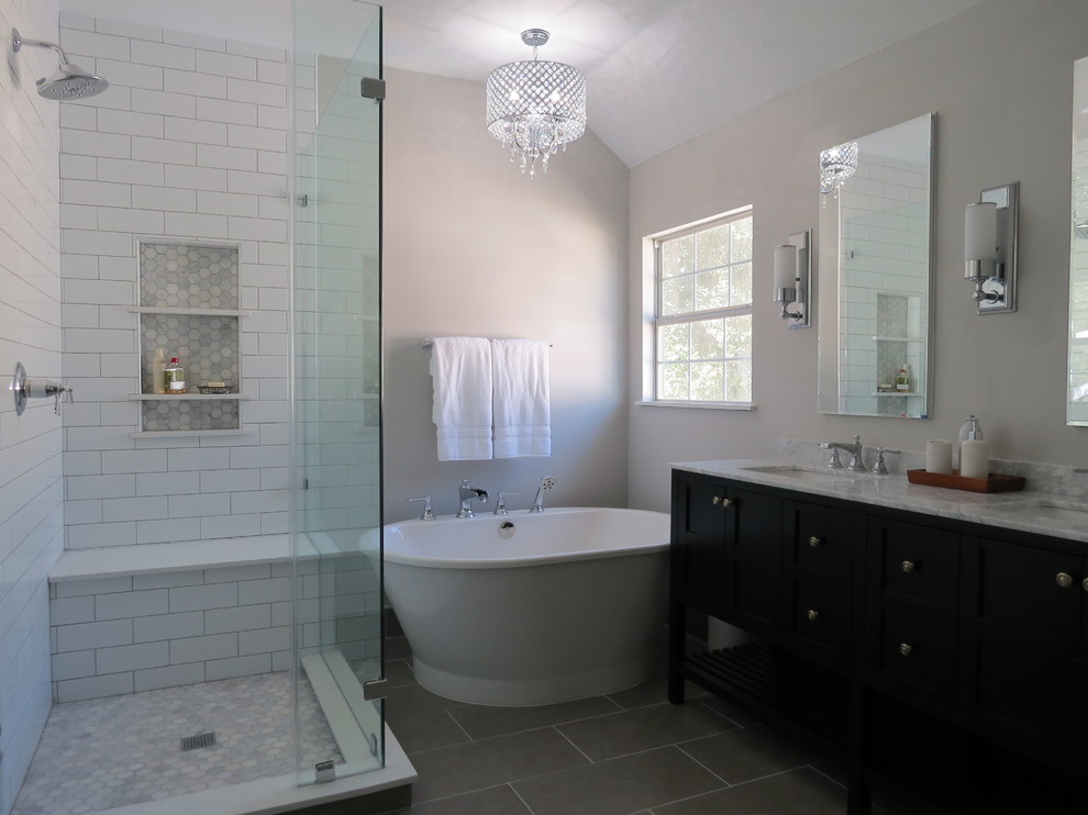 Design ideas for a large transitional master bathroom in Houston with furniture-like cabinets, black cabinets, a freestanding tub, a corner shower, white tile, ceramic tile, grey walls, porcelain floors, an undermount sink, marble benchtops, grey floor, a hinged shower door and white benchtops.