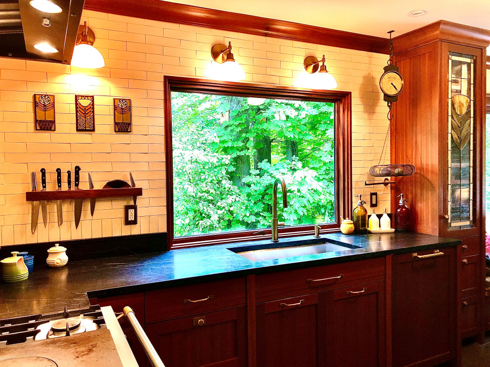 Photo of a mid-sized arts and crafts l-shaped separate kitchen in Seattle with an undermount sink, shaker cabinets, dark wood cabinets, soapstone benchtops, white splashback, subway tile splashback, coloured appliances, limestone floors, no island, black floor and black benchtop.