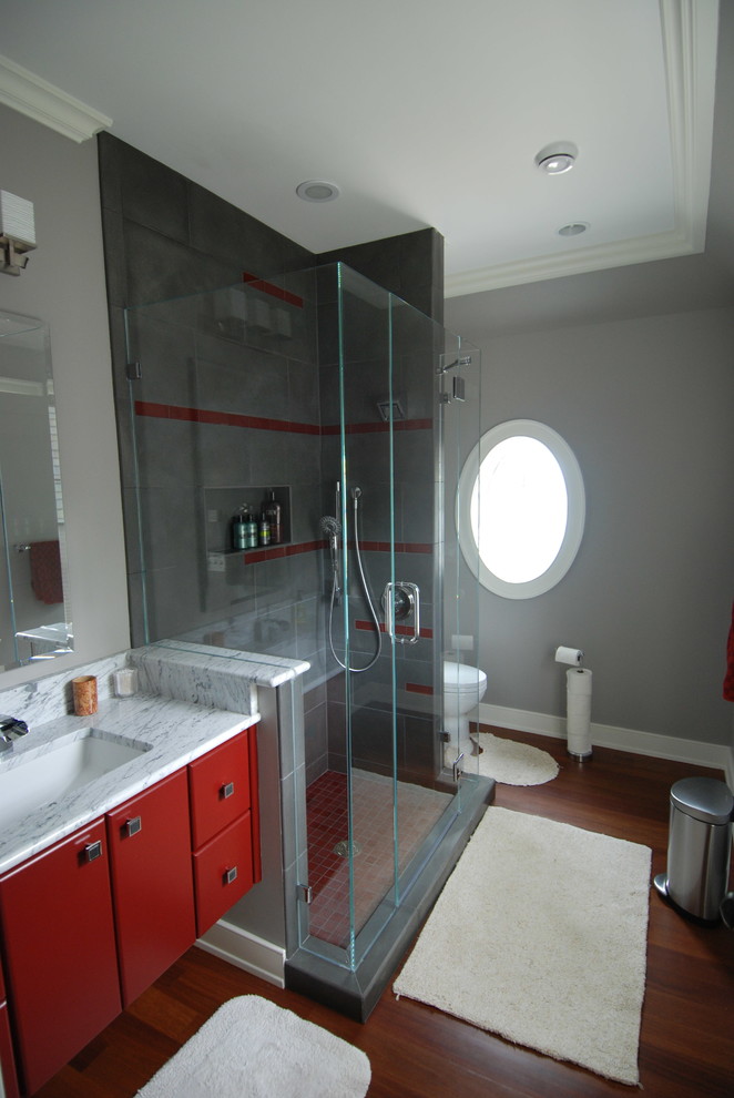 Mid-sized transitional kids bathroom in Milwaukee with an undermount sink, flat-panel cabinets, red cabinets, marble benchtops, an open shower, a two-piece toilet, gray tile, stone tile, grey walls and medium hardwood floors.