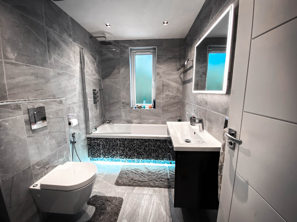 Inspiration for a medium sized modern grey and black family bathroom in London with black cabinets, a walk-in shower, a wall mounted toilet, grey tiles, porcelain tiles, grey walls, porcelain flooring, a wall-mounted sink, grey floors, a sliding door, a feature wall, a single sink and a floating vanity unit.