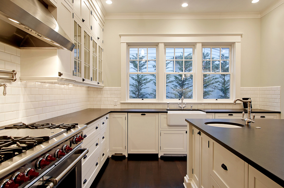Inspiration for a large traditional u-shaped kitchen in Seattle with shaker cabinets, stainless steel appliances, subway tile splashback, a farmhouse sink, white cabinets, white splashback and dark hardwood floors.