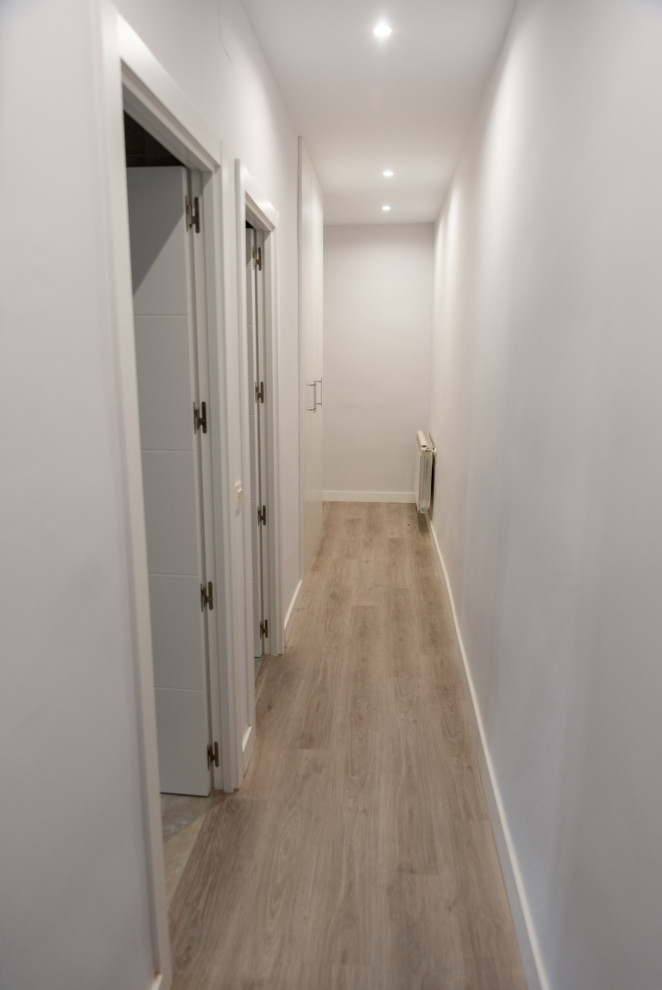 Photo of a mid-sized contemporary hallway in Madrid with white walls and light hardwood floors.