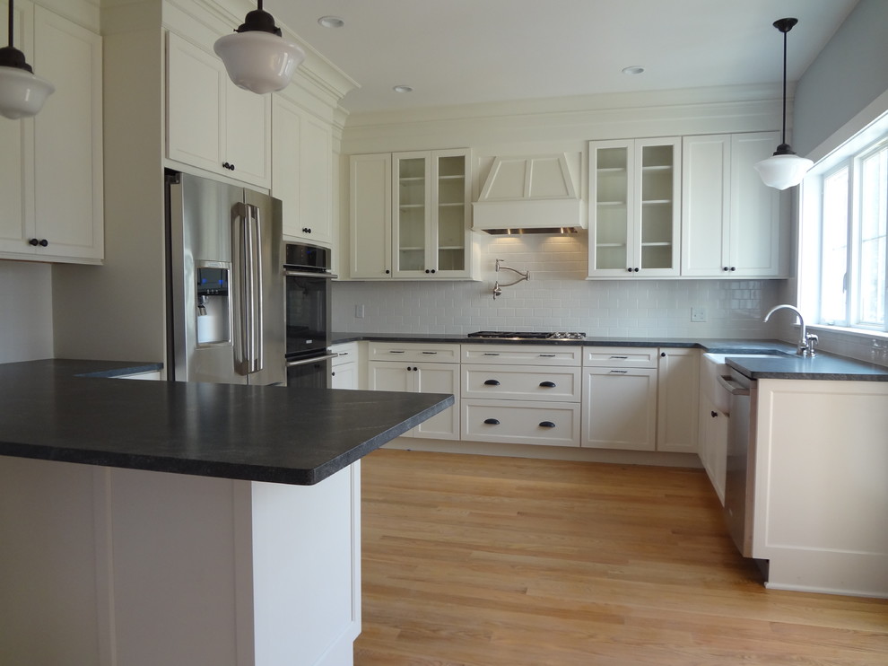 Eat-in kitchen - mid-sized transitional u-shaped light wood floor eat-in kitchen idea in Providence with a farmhouse sink, shaker cabinets, white cabinets, white backsplash, porcelain backsplash, stainless steel appliances and a peninsula