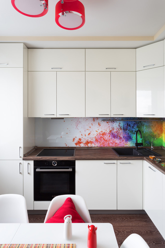This is an example of a mid-sized contemporary l-shaped separate kitchen in Moscow with flat-panel cabinets, white cabinets, laminate benchtops, multi-coloured splashback, glass sheet splashback, black appliances, vinyl floors, no island, brown floor and a drop-in sink.