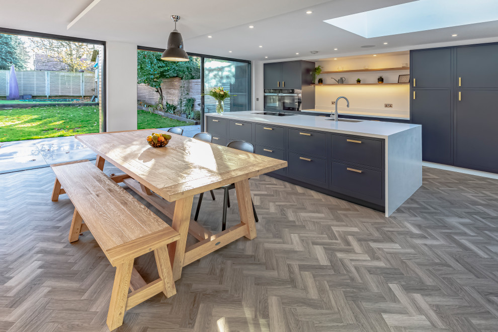 Design ideas for a mid-sized contemporary galley open plan kitchen in Kent with an undermount sink, flat-panel cabinets, blue cabinets, quartz benchtops, white splashback, panelled appliances, vinyl floors, with island, brown floor, white benchtop and recessed.