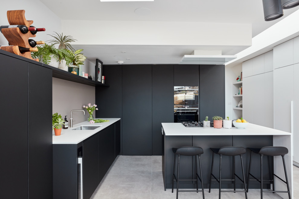 Design ideas for a mid-sized contemporary u-shaped eat-in kitchen in London with an integrated sink, flat-panel cabinets, black cabinets, quartz benchtops, pink splashback, glass sheet splashback, stainless steel appliances, with island and white benchtop.
