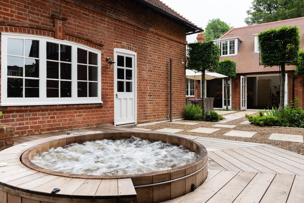 This is an example of a mid-sized traditional backyard round pool in London with natural stone pavers and a hot tub.