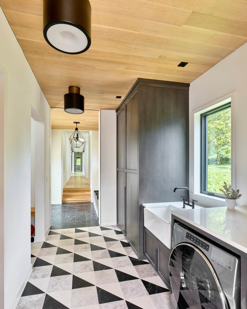 This is an example of a mid-sized modern l-shaped utility room in Philadelphia with a farmhouse sink, shaker cabinets, grey cabinets, quartz benchtops, marble floors, a side-by-side washer and dryer, multi-coloured floor, white benchtop and wood.