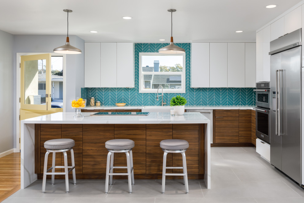 Large contemporary l-shaped eat-in kitchen in Los Angeles with a farmhouse sink, flat-panel cabinets, white cabinets, quartz benchtops, blue splashback, glass tile splashback, stainless steel appliances, porcelain floors, with island, grey floor and white benchtop.