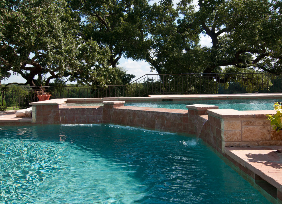 Inspiration for a large country backyard custom-shaped infinity pool in Houston with natural stone pavers and a water feature.