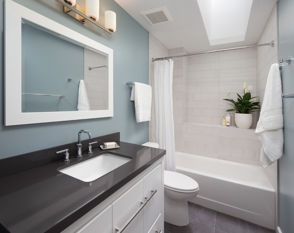 Mid-sized contemporary bathroom in DC Metro with a shower/bathtub combo, porcelain floors, grey floor, white cabinets, an alcove tub, a two-piece toilet, gray tile, porcelain tile, blue walls, an undermount sink, solid surface benchtops, grey benchtops and flat-panel cabinets.