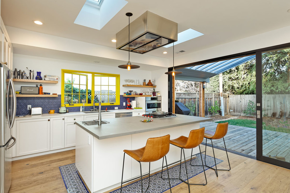 Contemporary l-shaped kitchen in San Francisco with an undermount sink, recessed-panel cabinets, white cabinets, blue splashback, stainless steel appliances, light hardwood floors, with island, beige floor and grey benchtop.