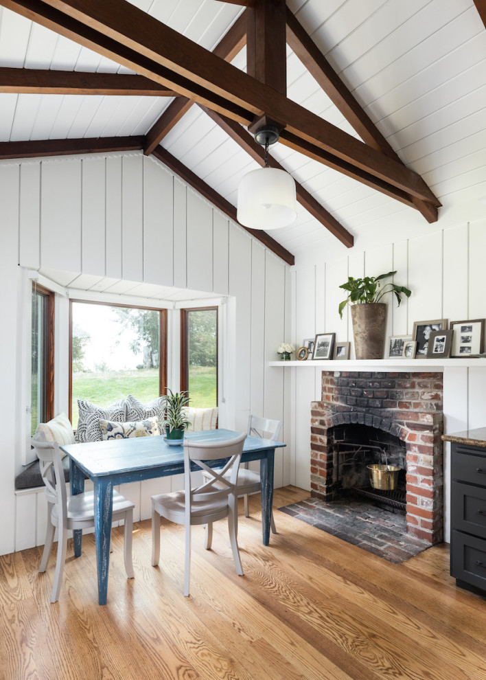 This is an example of a large rural dining room in San Francisco with banquette seating, white walls, a standard fireplace and exposed beams.