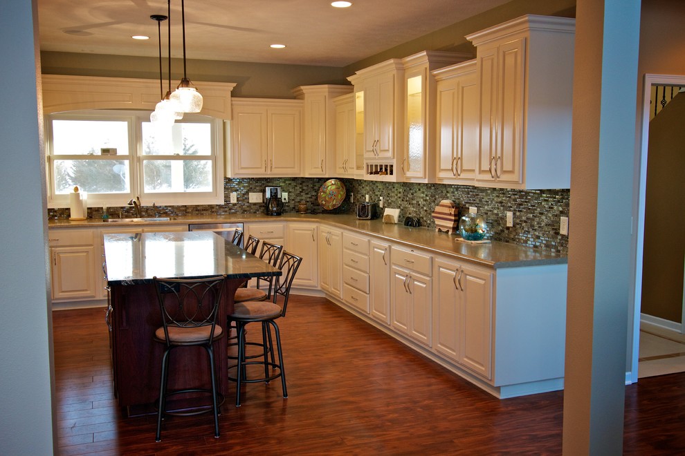 Large u-shaped medium tone wood floor open concept kitchen photo with a drop-in sink, raised-panel cabinets, white cabinets, multicolored backsplash, glass tile backsplash, stainless steel appliances and an island
