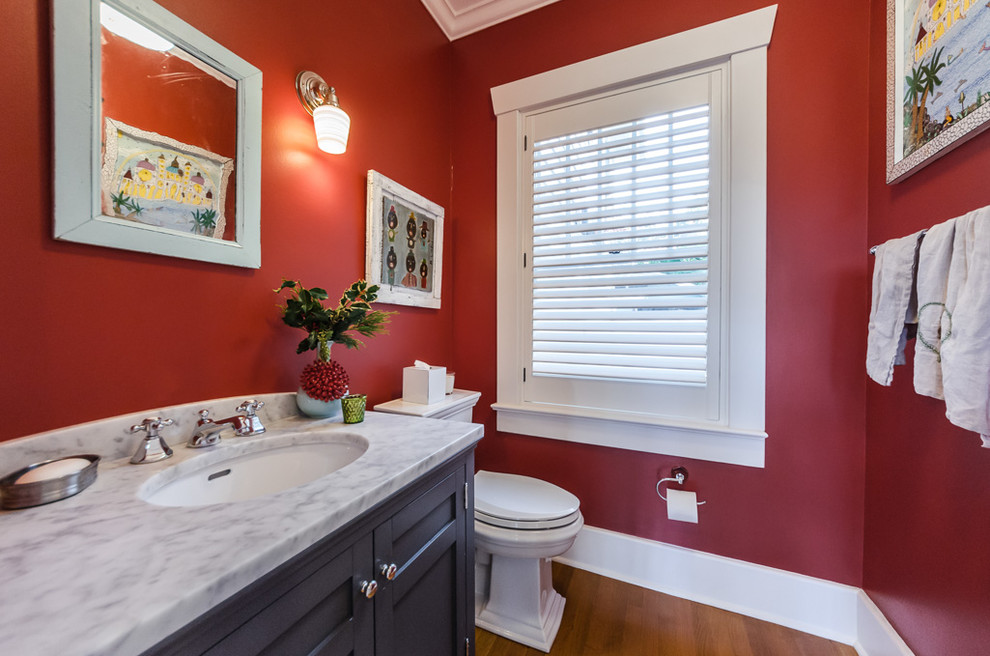 Photo of a traditional powder room in Tampa with recessed-panel cabinets, black cabinets, red walls, medium hardwood floors, an undermount sink, brown floor and grey benchtops.