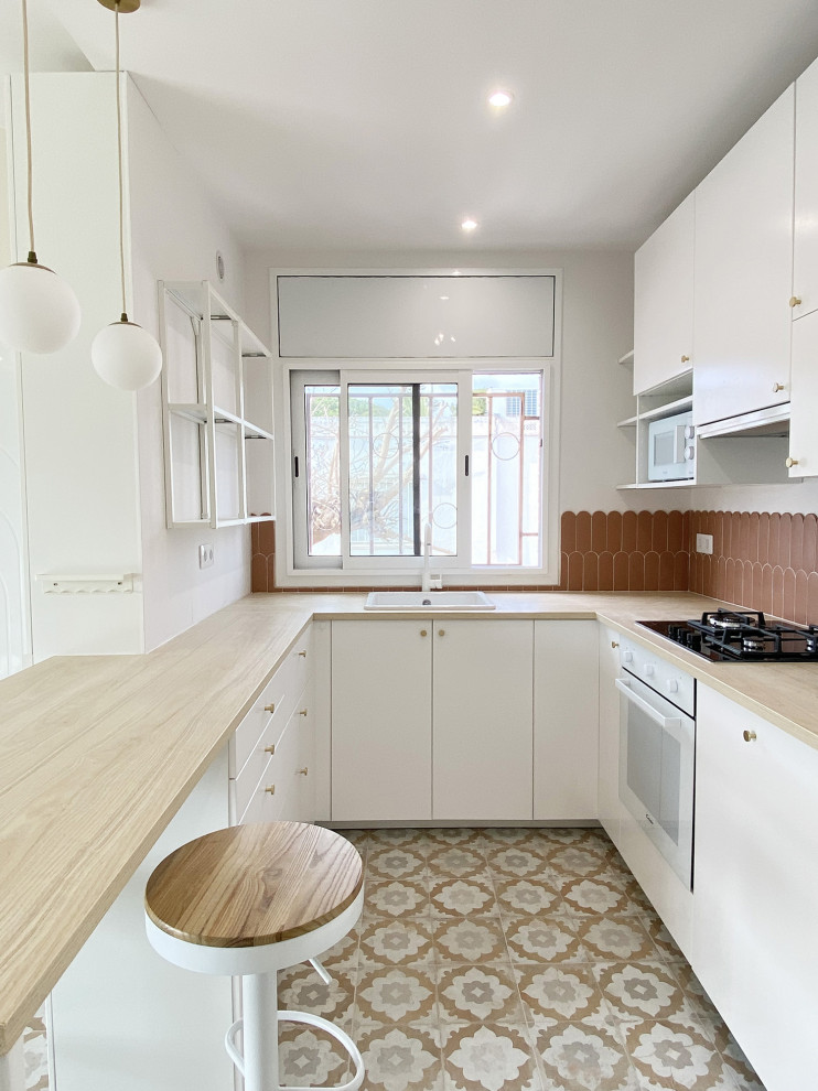 Cette image montre cuisine américaine in U With un évier 1 bac, un placard à porte plane, des portes de placard blanches, un plan de travail en bois, une crédence orange, une crédence en céramique, un électroménager blanc, carreaux de ciment au sol, îlot, un sol orange, un plan de travail beige and fenêtre au-dessus de l'évier.