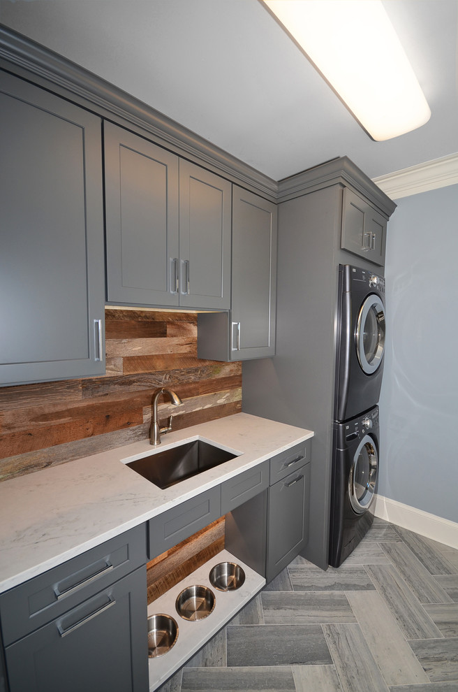 Inspiration for a mid-sized country dedicated laundry room in Charlotte with an undermount sink, shaker cabinets, grey cabinets, quartz benchtops, blue walls, limestone floors and a stacked washer and dryer.