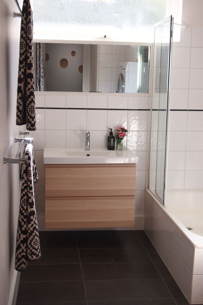 This is an example of a mid-sized contemporary kids bathroom in Melbourne with flat-panel cabinets, light wood cabinets, a drop-in tub, a shower/bathtub combo, white tile, ceramic tile, white walls, ceramic floors, grey floor and a hinged shower door.
