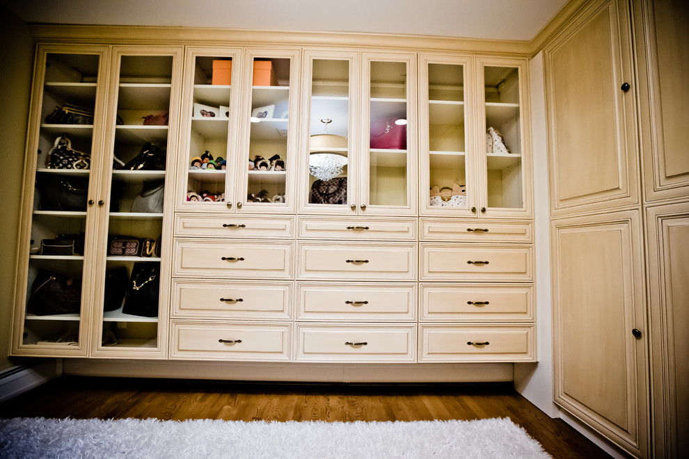 This is an example of a large traditional women's walk-in wardrobe in New York with raised-panel cabinets, white cabinets, medium hardwood floors and brown floor.