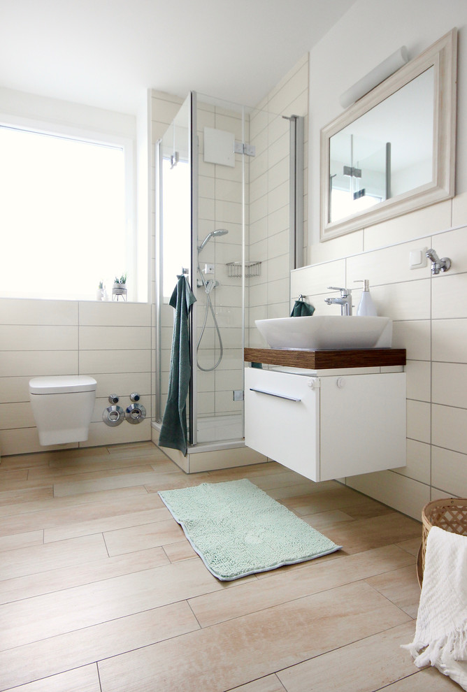 Photo of a mid-sized contemporary 3/4 bathroom in Frankfurt with flat-panel cabinets, white cabinets, a corner shower, a wall-mount toilet, white tile, porcelain tile, white walls, cement tiles, a vessel sink, wood benchtops, beige floor, a hinged shower door and brown benchtops.