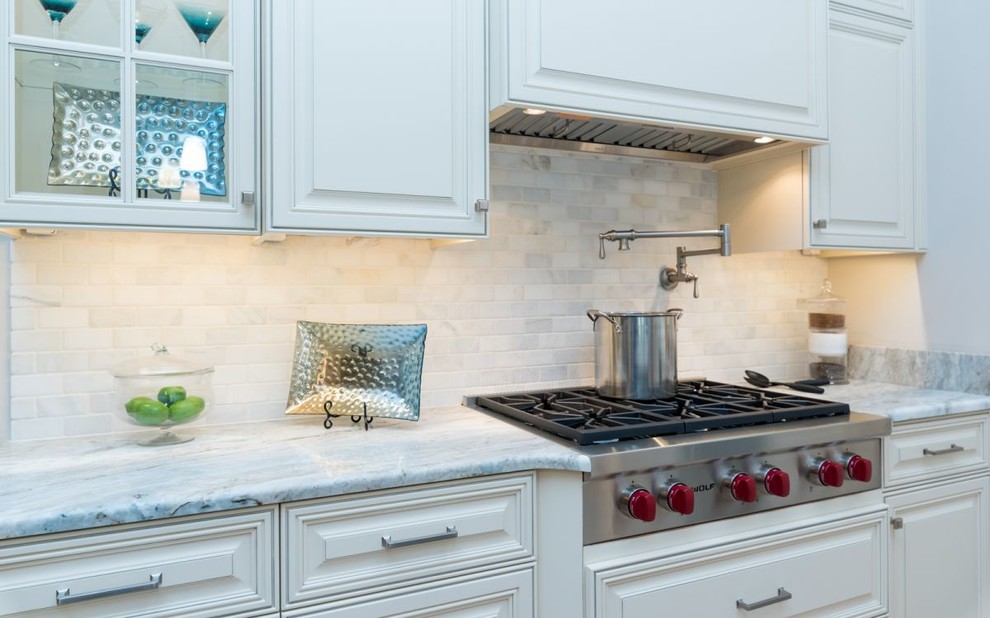 Mid-sized traditional u-shaped open plan kitchen in Tampa with an undermount sink, raised-panel cabinets, white cabinets, marble benchtops, white splashback, stone tile splashback, stainless steel appliances, light hardwood floors and with island.