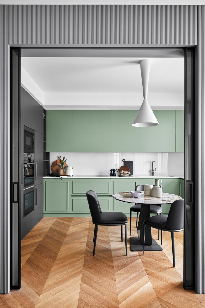 Moderne Wohnküche in L-Form mit Doppelwaschbecken, grünen Schränken, Mineralwerkstoff-Arbeitsplatte, Küchenrückwand in Weiß, Glasrückwand, hellem Holzboden und weißer Arbeitsplatte in Mailand