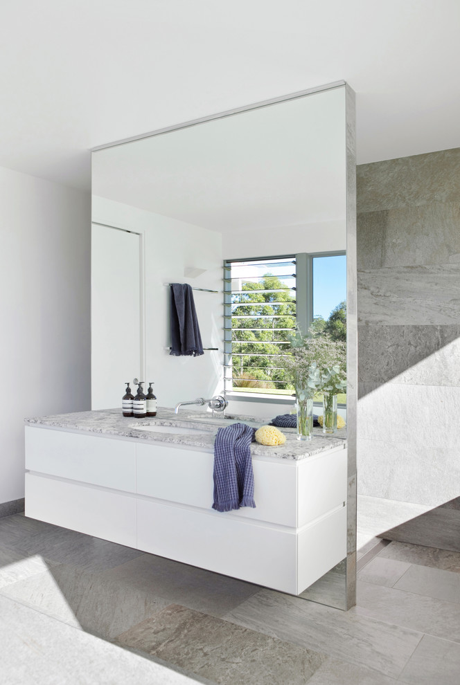 Inspiration for a mid-sized modern master bathroom in Sunshine Coast with white cabinets, a wall-mount toilet, gray tile, porcelain tile, white walls, porcelain floors, an undermount sink, granite benchtops, grey floor, an open shower, grey benchtops and flat-panel cabinets.
