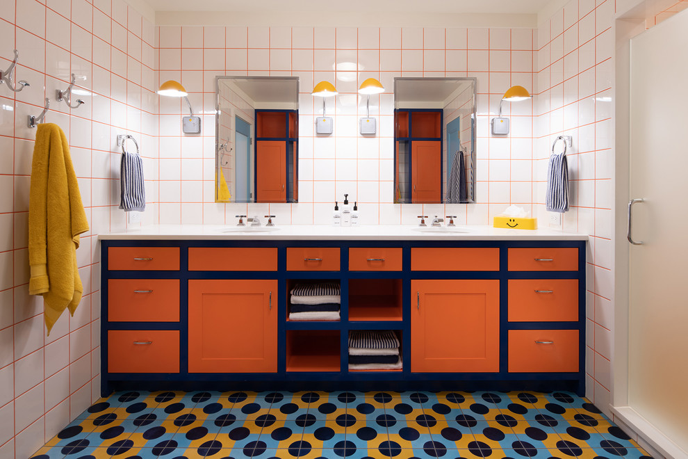 Eclectic bathroom in Minneapolis with shaker cabinets, orange cabinets, an alcove shower, white tile, white walls, an undermount sink, multi-coloured floor, a hinged shower door and white benchtops.
