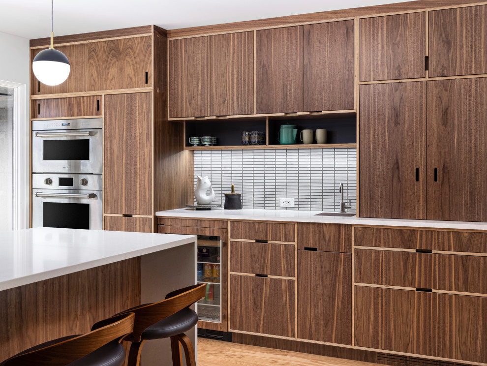 Inspiration for a midcentury l-shaped eat-in kitchen in Detroit with white splashback, with island, white benchtop, an undermount sink, flat-panel cabinets, dark wood cabinets, quartz benchtops, mosaic tile splashback, stainless steel appliances and medium hardwood floors.