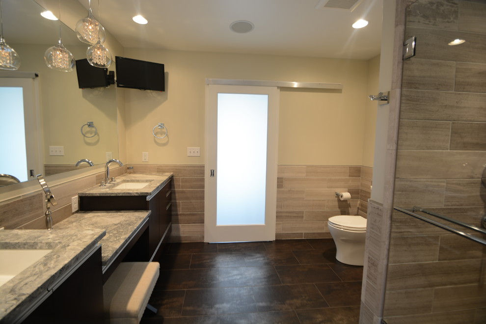 Design ideas for a large contemporary master bathroom in Milwaukee with an undermount sink, flat-panel cabinets, dark wood cabinets, granite benchtops, a drop-in tub, a double shower, a one-piece toilet, gray tile, stone tile, beige walls and porcelain floors.