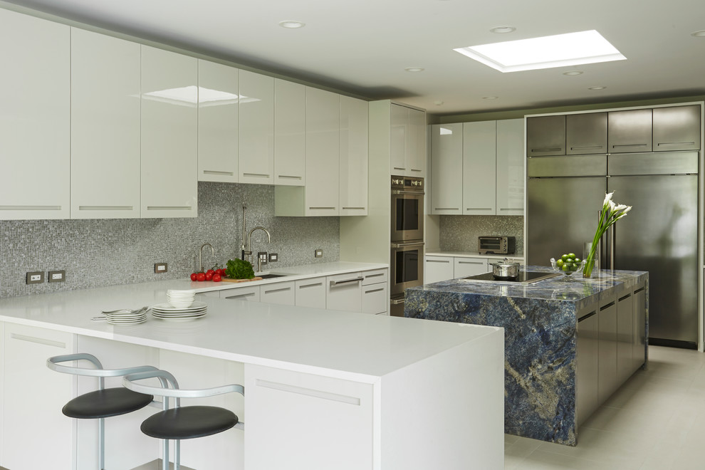 Photo of a large modern u-shaped kitchen in Chicago with an undermount sink, flat-panel cabinets, white cabinets, solid surface benchtops, grey splashback, mosaic tile splashback, stainless steel appliances, porcelain floors, with island and beige floor.