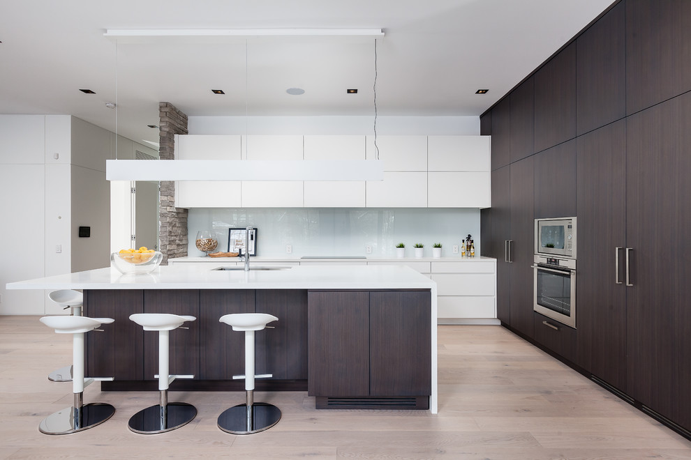 Photo of a large contemporary l-shaped kitchen in Toronto with an undermount sink, flat-panel cabinets, white cabinets, white splashback, glass sheet splashback, stainless steel appliances, light hardwood floors, with island and beige floor.