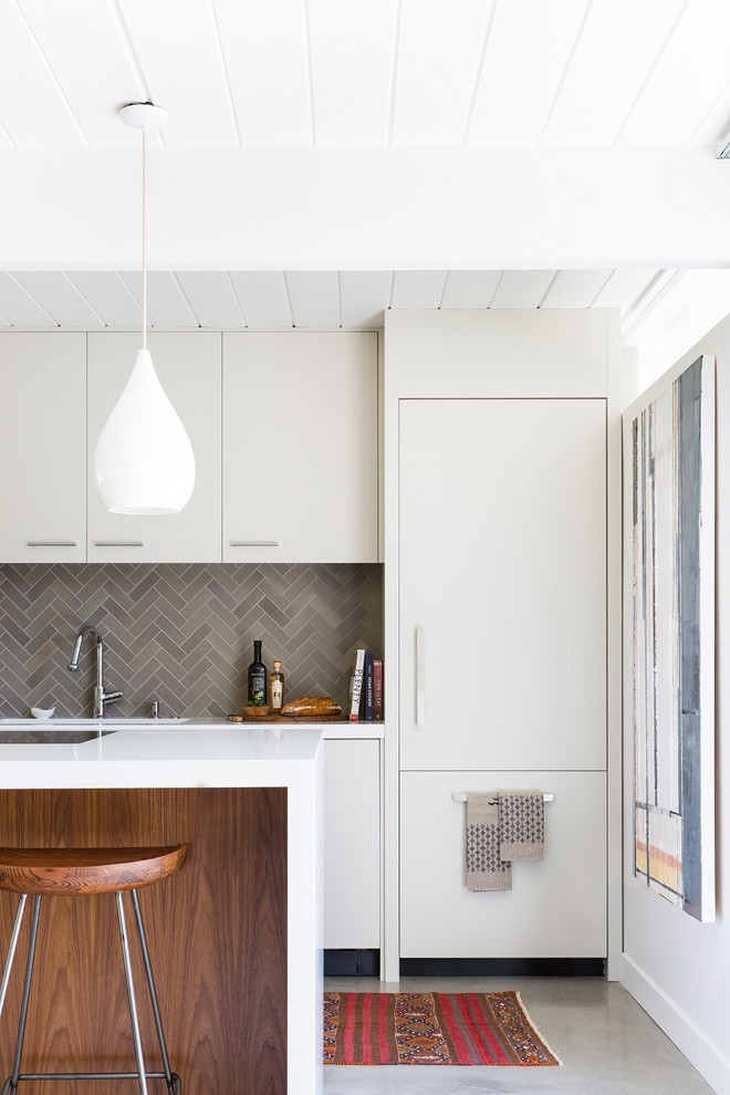 This is an example of a midcentury single-wall kitchen in San Francisco with an integrated sink, flat-panel cabinets, white cabinets, grey splashback, ceramic splashback, white appliances, concrete floors, with island and quartz benchtops.
