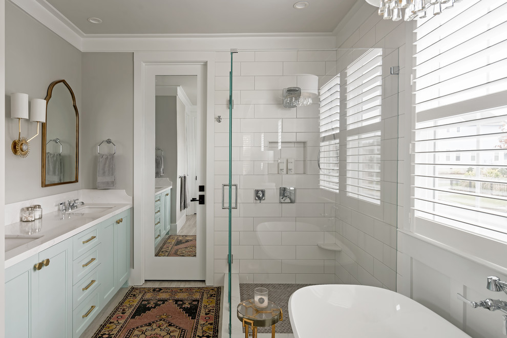 Inspiration for a mid-sized transitional master bathroom in Charlotte with recessed-panel cabinets, turquoise cabinets, a freestanding tub, a corner shower, white tile, ceramic tile, grey walls, porcelain floors, an undermount sink, engineered quartz benchtops, grey floor, a hinged shower door, white benchtops, a bidet, a niche, a double vanity, a built-in vanity and decorative wall panelling.