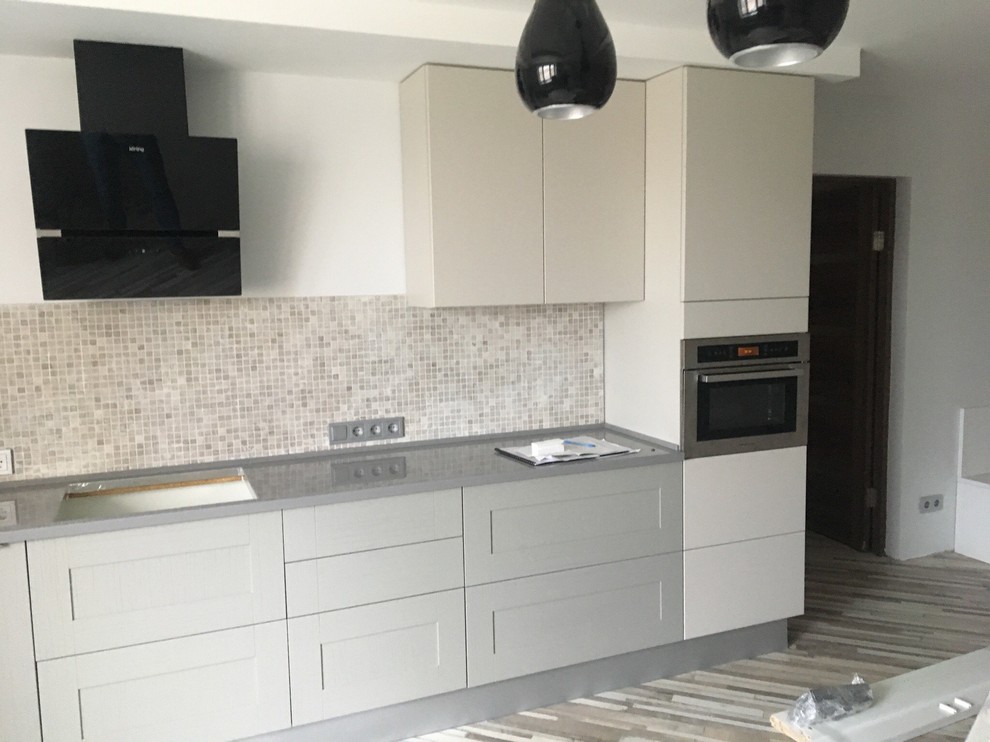 Photo of a large transitional galley eat-in kitchen in Moscow with an integrated sink, raised-panel cabinets, grey cabinets, solid surface benchtops, multi-coloured splashback, mosaic tile splashback, black appliances, with island and grey benchtop.