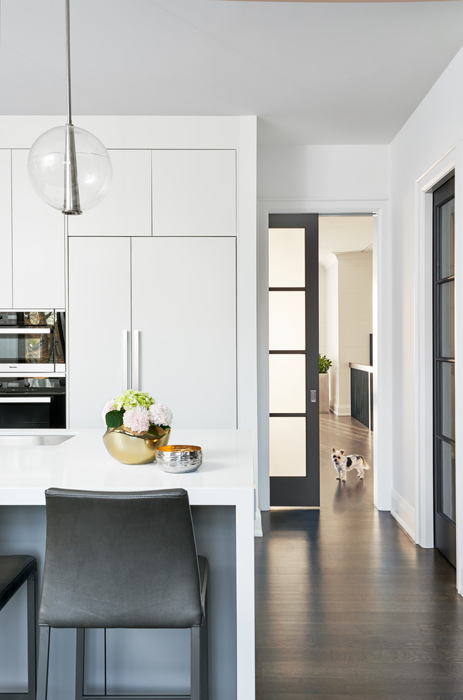 This is an example of a mid-sized contemporary l-shaped open plan kitchen in Toronto with an undermount sink, white cabinets, quartz benchtops, stainless steel appliances, dark hardwood floors, with island, brown floor and flat-panel cabinets.