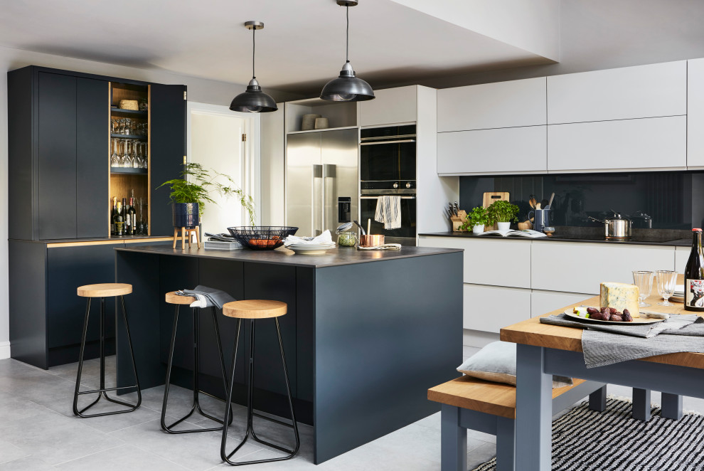 Large contemporary l-shaped eat-in kitchen in London with blue cabinets, blue splashback, glass sheet splashback, panelled appliances, with island, grey floor and black benchtop.