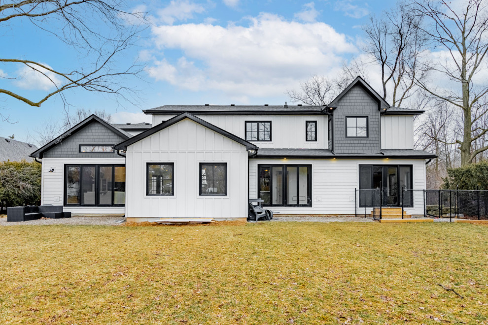 Large country concrete white house exterior in Toronto with a gable roof, a mixed roof, a black roof and board and batten siding.