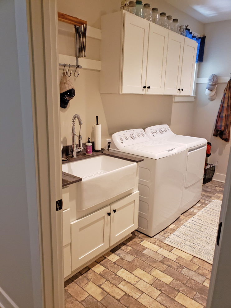 Example of a large farmhouse single-wall ceramic tile and multicolored floor utility room design in Nashville with a farmhouse sink, shaker cabinets, white cabinets, granite countertops, beige walls, a side-by-side washer/dryer and gray countertops